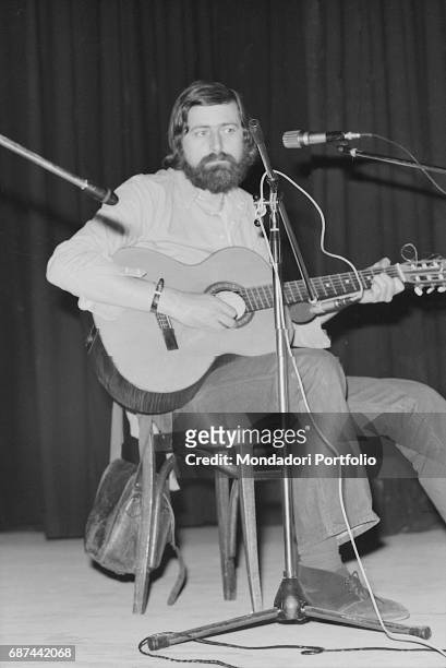 Italian singer and writer Francesco Guccini sitting with a guitar and a mic while performing on stage at Teatro Quartiere in Quarto Oggiaro, northern...