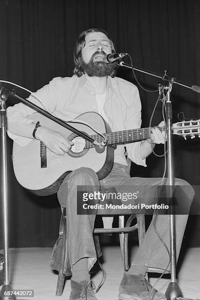 Italian singer and writer Francesco Guccini sitting with a guitar and a mic while performing on stage at Teatro Quartiere in Quarto Oggiaro, northern...