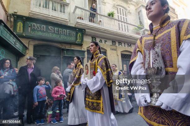 Young women wearing ceremonial altar server robes hold religious objects during a Semana Santa procession in the historic center of Càdiz.