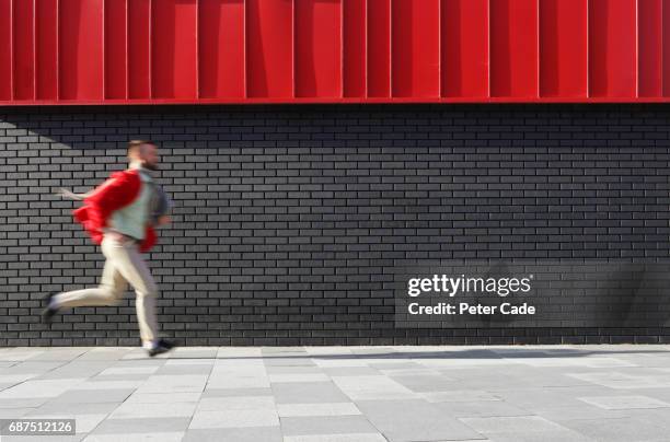 man running next to black and red building - red wall stock pictures, royalty-free photos & images