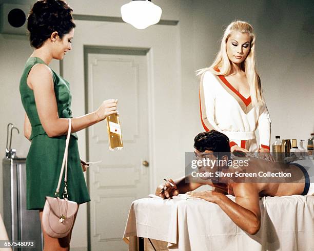 American actor and singer Dean Martin receives a bottle of whisky from actress Beverly Adams during a massage, in a scene from the comedy film 'The...