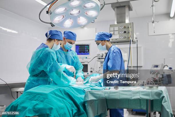 team of surgeons in operating room at a hospital. - sala de cirurgia com assistência imagens e fotografias de stock