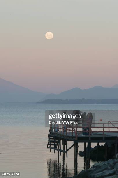 Tourists on Dock watching Moon, Puerto Varas, Chile with Osorno Volcano and Llanquihue Lake.