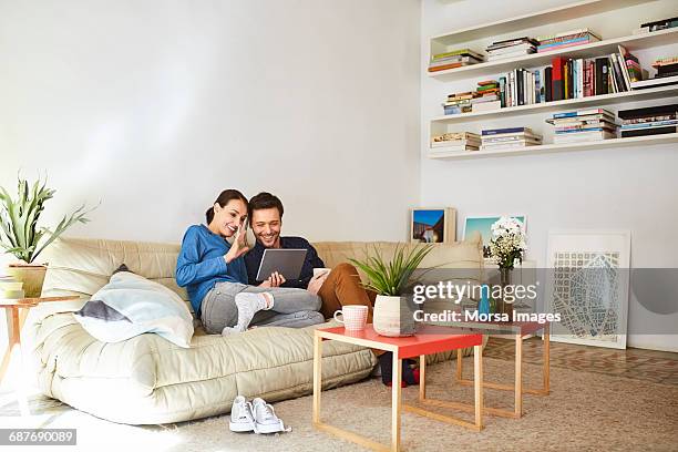 happy couple video chatting on digital tablet - couple on sofa stockfoto's en -beelden