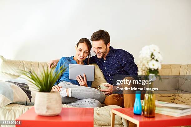 couple using digital tablet on sofa at home - happy couple computer stock pictures, royalty-free photos & images