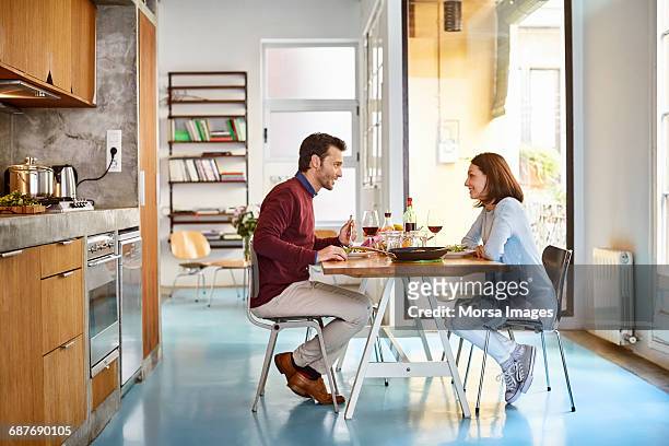 mid adult couple sitting at dining table - eettafel stockfoto's en -beelden