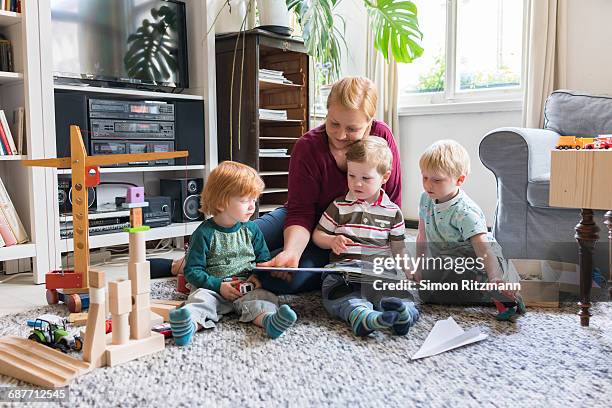 mother with three toddler boys reading storybook - stories of the day stock-fotos und bilder