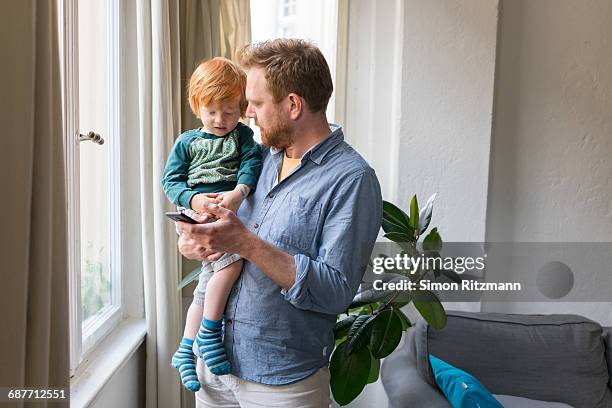 father holding toddler son using mobile phone - leanincollection dad stock pictures, royalty-free photos & images