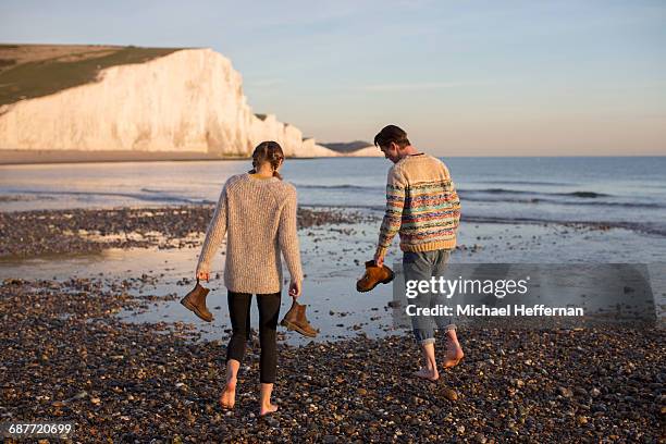 couple walking bare foot on beach - jeans back stockfoto's en -beelden