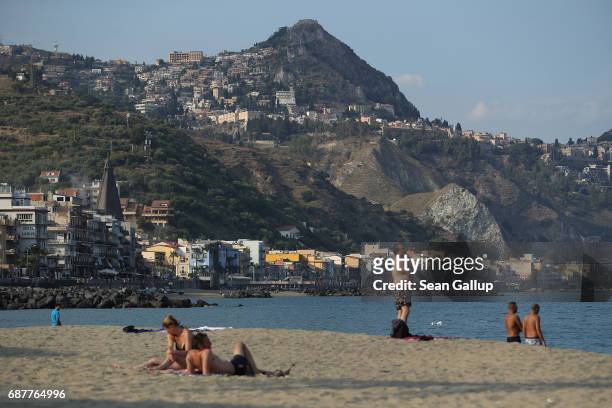 People relax on a beach as the historic town of Taormina, which will host the upcoming G7 summit, stands perched on rocks behind on the island of...