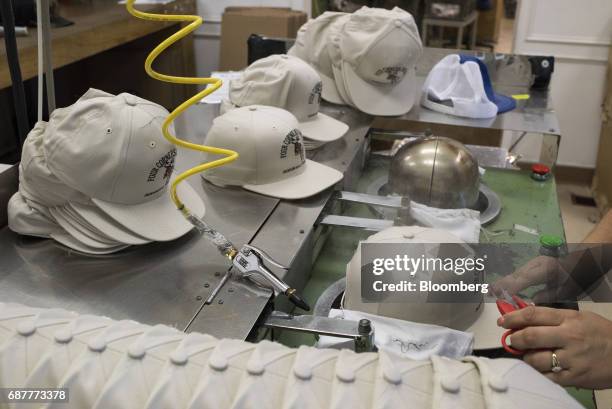 An employee uses steam to shape baseball hats coming off the manufacturing line at the Graffiti Caps production facility in Cleveland, Ohio, U.S., on...