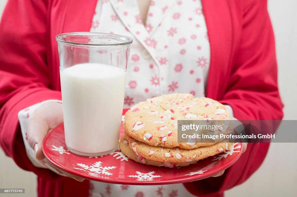 Woman holding Christmas cookies and glass of milk on plate