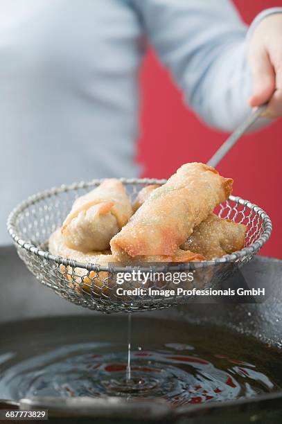 taking deep-fried spring rolls out of wok - schuimspatel stockfoto's en -beelden