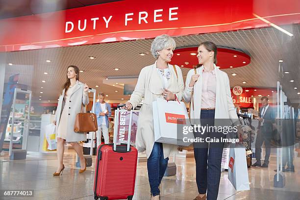 women leaving airport duty free shop with shopping bags and suitcase - airport shop stock-fotos und bilder