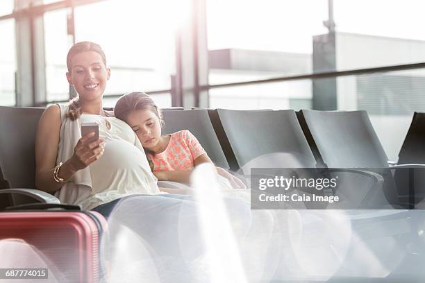 pregnant mother with cell phone and sleeping daughter in airport departure area - airport smartphone stock pictures, royalty-free photos & images