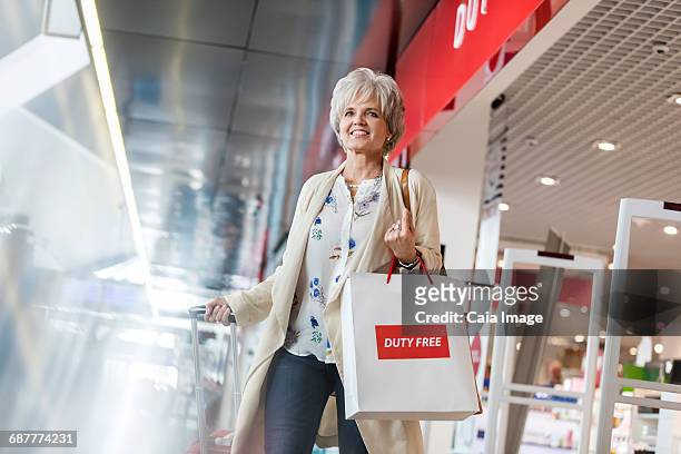 smiling woman leaving airport duty free shop with shopping bag - duty free photos et images de collection