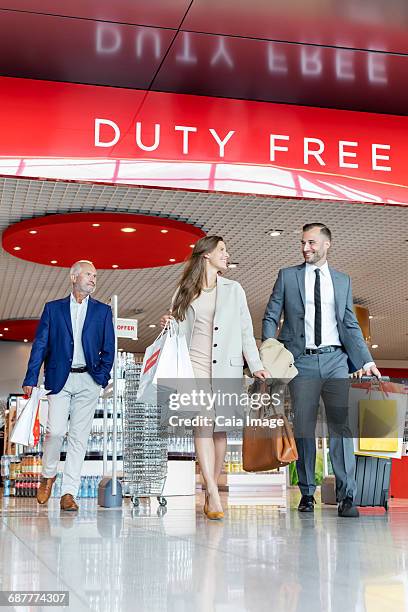 business people leaving airport duty free shop with shopping bags and suitcase - duty free photos et images de collection