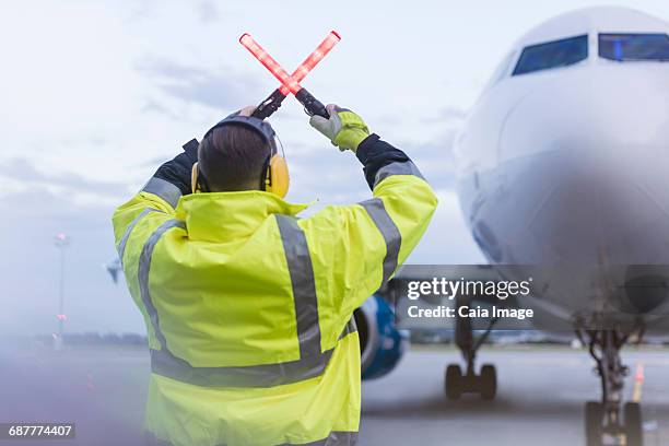 air traffic controller guiding airplane with wand lights on tarmac - air traffic control stock-fotos und bilder