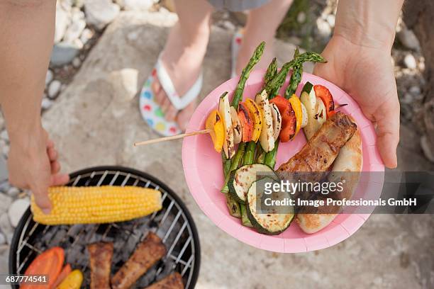 woman holding plate of grilled food at barbecue on river bank - paper plate 個照片及圖片檔