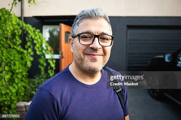 smiling man wearing eyeglasses standing against house - arab man smiling stock-fotos und bilder