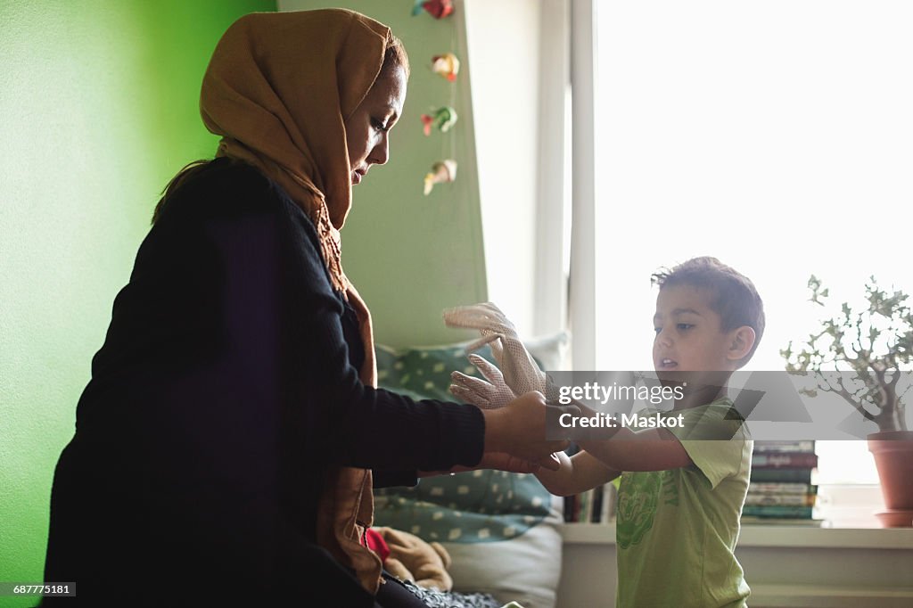 Mother putting gloves on sons hand in bedroom