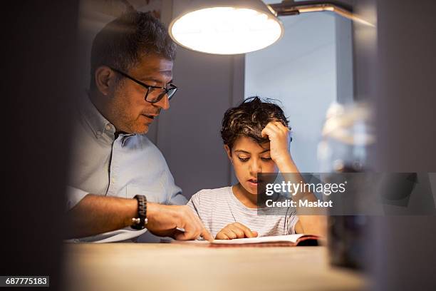 Father and son reading book in darkroom at home