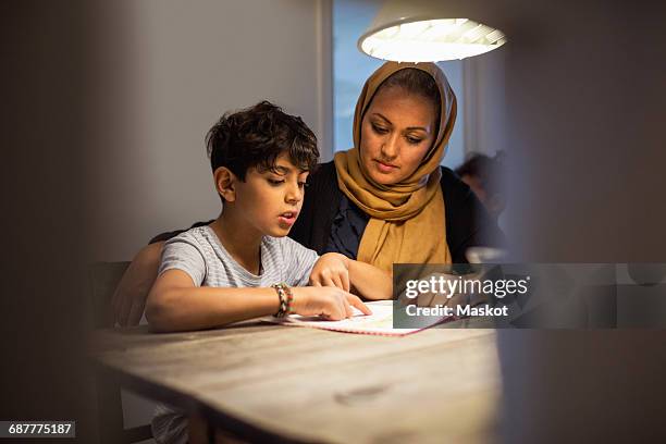 mother and son reading book in darkroom at home - muslim boy stockfoto's en -beelden