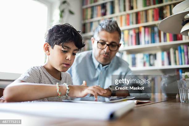 father assisting son in using digital tablet while studying at brightly lit home - two young arabic children only indoor portrait stock-fotos und bilder