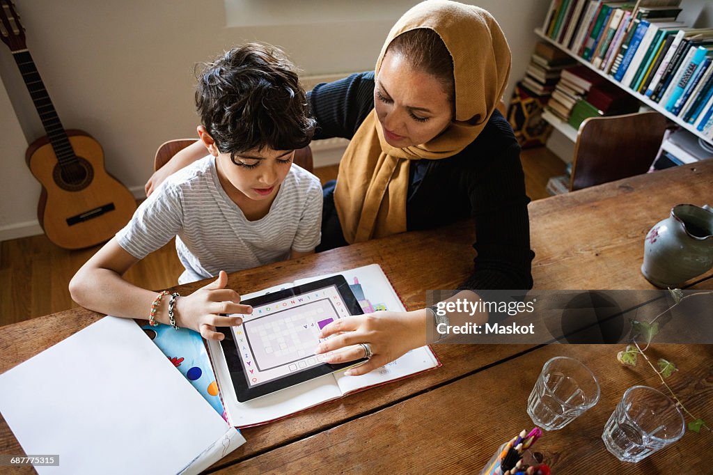 High angle view of mother assisting son in using digital tablet while studying at home