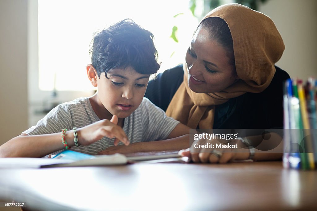 Smiling mother assisting son in using digital tablet while studying at home