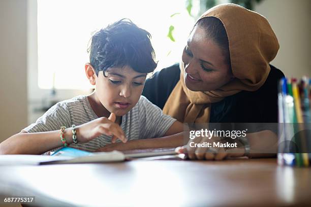 smiling mother assisting son in using digital tablet while studying at home - two young arabic children only indoor portrait stock-fotos und bilder