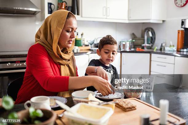 mother and son having breakfast at dining table in kitchen - mother and child snacking stockfoto's en -beelden