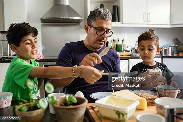 father and sons applying butter on crackers at dining table - butter knife stock pictures, royalty-free photos & images