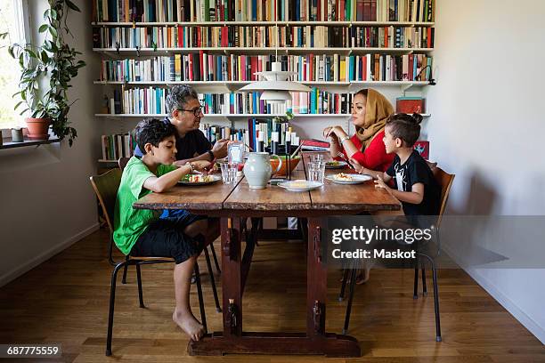 family having meal at table by bookshelf - headscarf home stockfoto's en -beelden