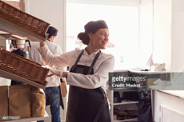 happy female owner looking away while standing by shelves in brightly lit grocery store - uniform werk stockfoto's en -beelden