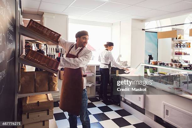 male owner looking away while standing by shelves in brightly lit grocery store - grocery store window stock pictures, royalty-free photos & images