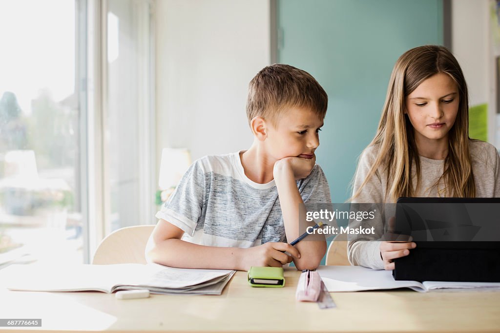 Boy looking while girl using tablet at desk in classroom