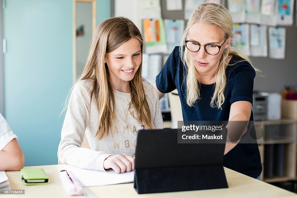 Teacher assisting happy girl in using digital tablet at school