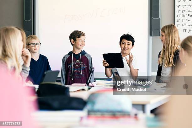 happy boy giving presentation with digital tablet amidst students in classroom - interactive whiteboard foto e immagini stock