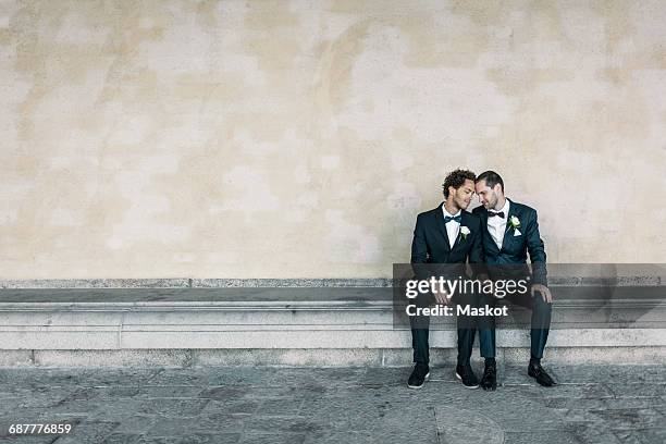 newlywed gay couple sitting on bench against wall - civil partnership stock pictures, royalty-free photos & images