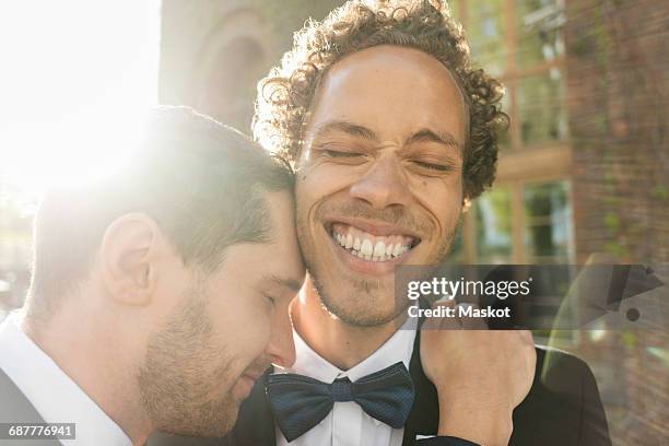 close-up of gay man embracing cheerful newlywed partner with eyes closed - eventos de la vida fotografías e imágenes de stock