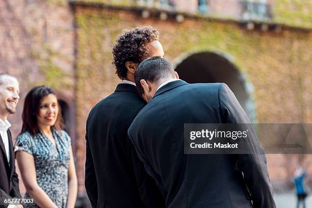 rear view of gay man leaning on partners shoulder during wedding ceremony - civil partnership stock pictures, royalty-free photos & images