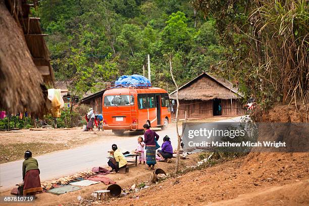 a tour bus drives through a local village. - oudomxai stock pictures, royalty-free photos & images