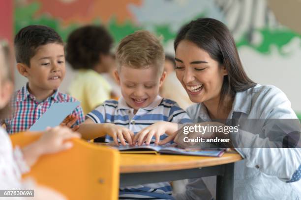 glückliche lehrer mit einem schüler an der schule ein buch lesen - preschool classroom stock-fotos und bilder