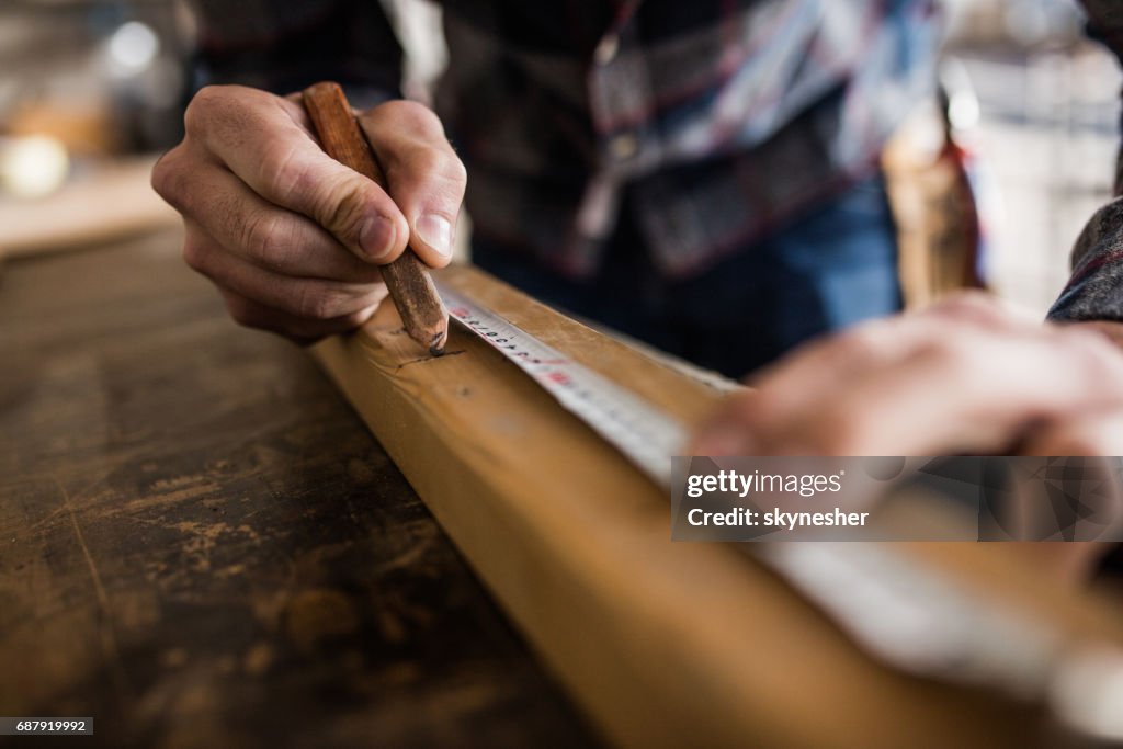 Cerca de carpintero irreconocible las medidas en una pieza de madera de la marca.