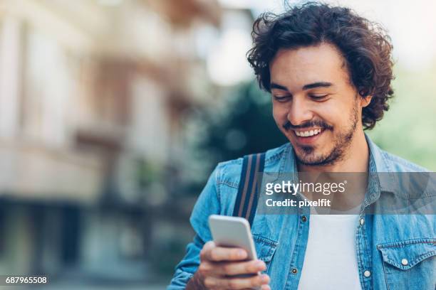 smiling man with smart phone - young men walking stock pictures, royalty-free photos & images