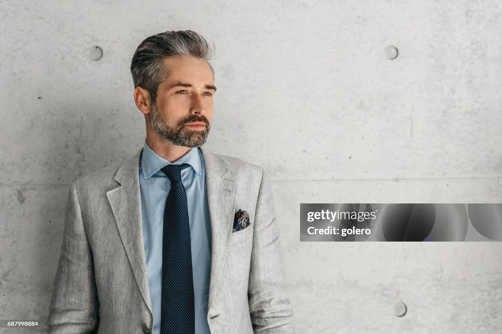 Handsome bearded businessman standing in front of concrete wall