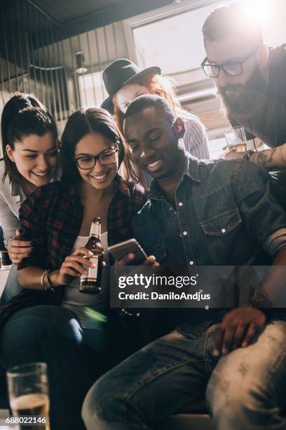 groep vrienden met plezier in een bar en spelen met de smartphone - sun flare on glass stockfoto's en -beelden