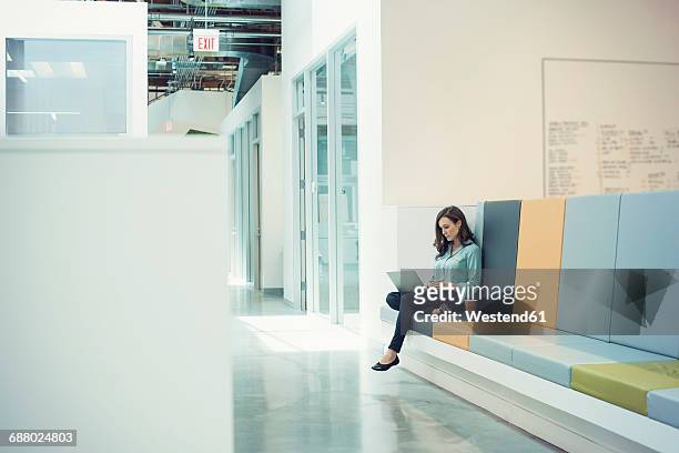 young businesswoman sitting on bench, using laptop - white bench stock pictures, royalty-free photos & images