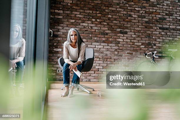 woman with long grey hair sitting on chair at the window - focus on background stock-fotos und bilder